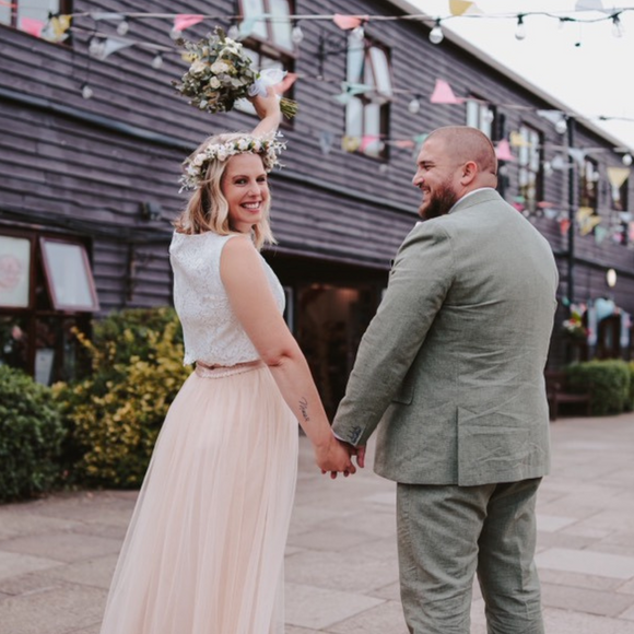 A Bride holding her Groom's hand in a rustic setting. Bride is wearing a cropped Lace Wedding Top and a champagne tulle bridal skirt.