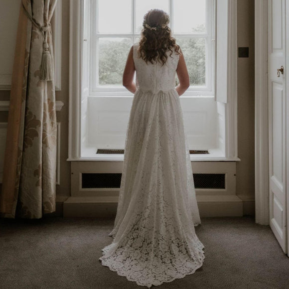 The back of a bride looking out of a sash window. The Bride s wearing a sleeveless lace top with a lace skirt with a train.