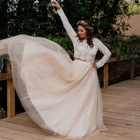 A bride wearing a long sleeve lace top and a full champagne tulle skirt. Bride is flicking up the skirt to show the size of the