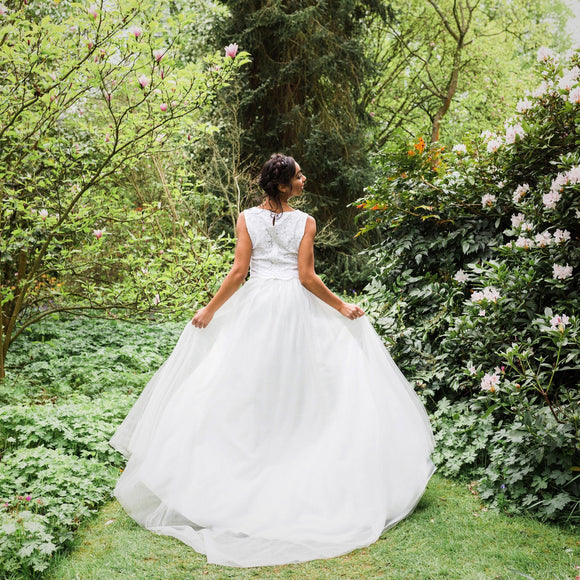 A bride in a white tulle full wedding skirt with a floral background, standing in a garden.
