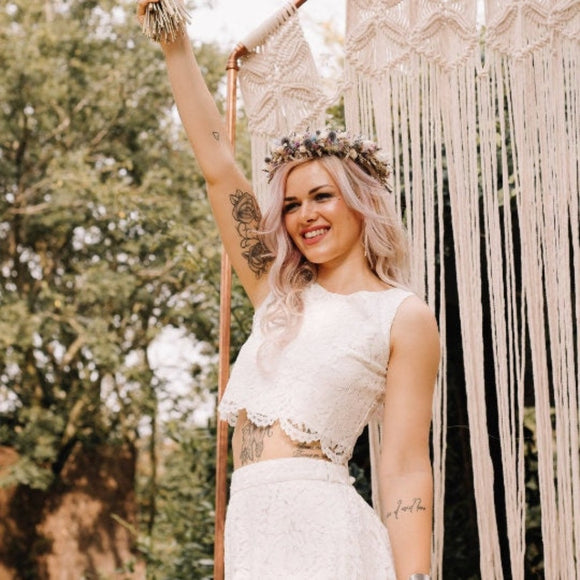 A woman wearing a white bridal lace top with a sleeveless design, paired with a matching skirt, standing outdoors.