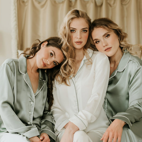 Three women in matching green and white pajama sets sitting together in a bedroom.